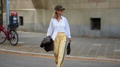 FRANKFURT AM MAIN, GERMANY - APRIL 21: Yvonne Schuppler-Kammerer is seen holding a dark brown leather blazer from Stradivarius; wearing an oversized white button down shirt from Zara; pale yellow wide leg track trousers with black three-stripe detail from Adidas; black pointed toe slingback pumps from H&M; a dark brown FF monogram canvas 